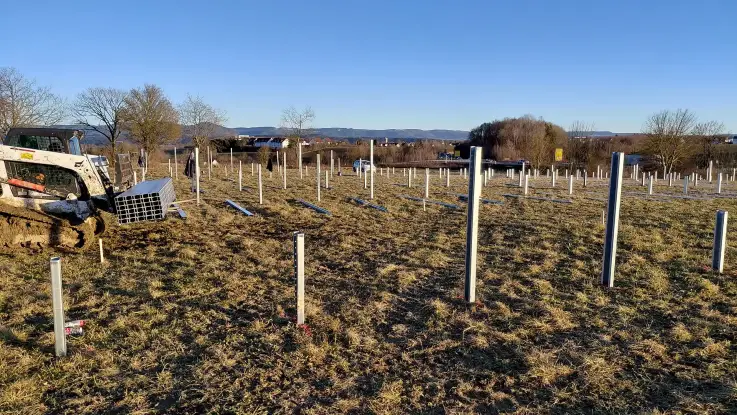 Links im Bild ein Raupenfahrzeug, auf der Solarparkfläche sind viele Träger für die PV-Module bereits verankert.
