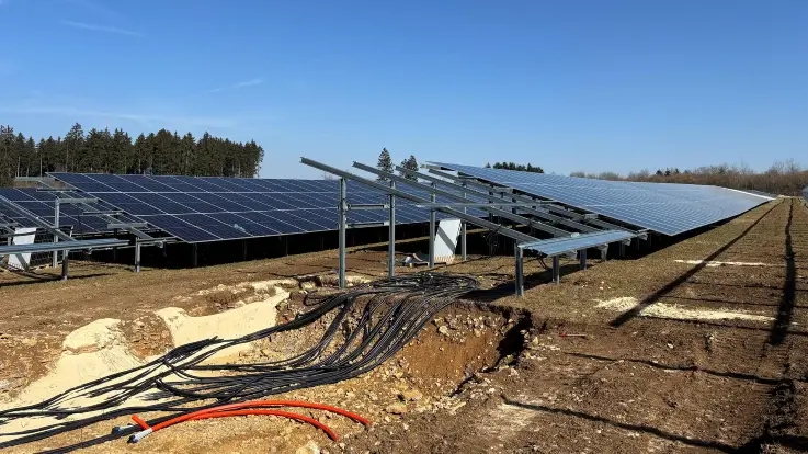 Die PV-Module sind nun fast vollständig auf den Gestellen montiert, darunter zahlreiche Kabelstränge, die noch unter die Erde verbracht werden müssen.