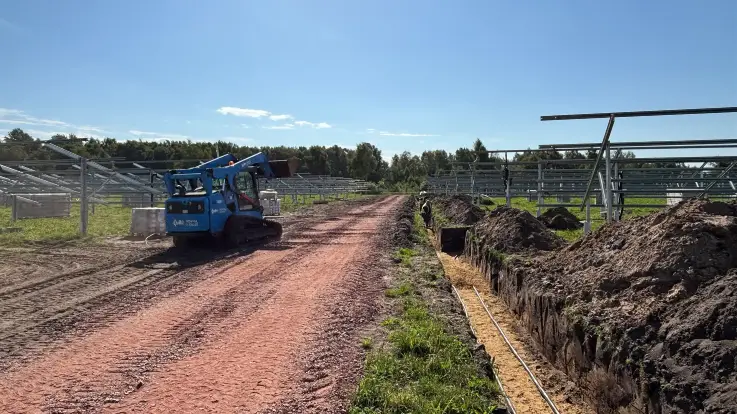 Gestelle für die Montage von PV-Modulen, ein Bagger sowie ein Graben, in dem Leitungen liegen