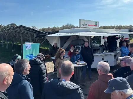 Inmitten eines Solarparks ein Imbisswagen, umgeben von Menschen, an einem Stehpult diie Organisatoren des Solarparks.