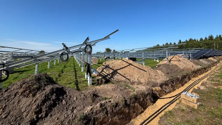 Kabel in Gräben werden mit den Gestellen für die PV-Module verbunden, im Hintergrund sind die ersten Module schon montiert.