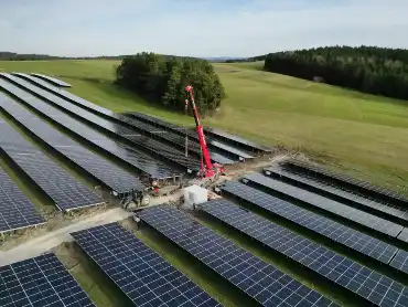 Luftaufname von Wiesen- und Feldflächen, dahinter sind ein Dorf und bewaldete Hügel zu erkennen