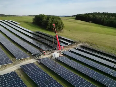 Zwischen dem Modulreihen eines Solarparks platziert ein Schwerlastkran einen kleinen Bau aus Beton an einem Weg zwischen den Reihen.