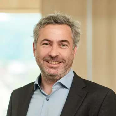 Alexander Sladek in einem Flur, der in lichten Holztönen gehalten ist