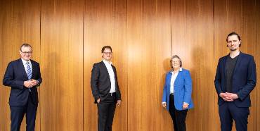 Vor einer Holzwand stehen eine Frau und drei Männer