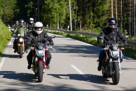 Gruppe von E-Motorradfahrern auf der Straße in einem Waldabschnitt