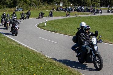 Ein E-Motorradfahrer legt sich in die Kurve, im Hintergrund ein Windrad