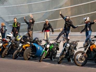 Eine Reihe Elektromotorräder, dahinter die Fahrer, gekleidet in Motorradmontur, in Jubelposen