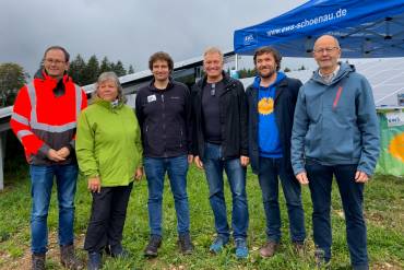 Fünf Menschen stehen nebeneinander auf einem Feld vor einem Pavillonzelt