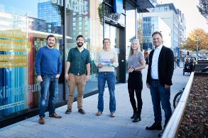 Gruppenfoto von fünf Menschen vor einem großen Gebäude mit Glasfassade