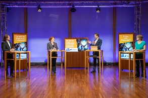 Zwei Männer und zwei Frauen stehen an Pulten in einer Diskussionsrunde