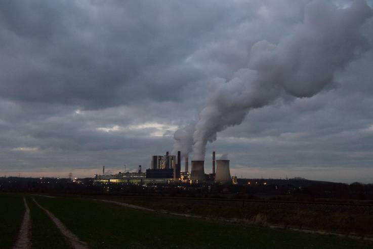 Am Horizont unter dunklem Himmel ein Kohlekraftwerk, dem große Schwaden entsteigen.