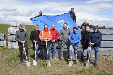 Gruppe steht mit Spaten vor einem Banner der EWS und Baumaterialien