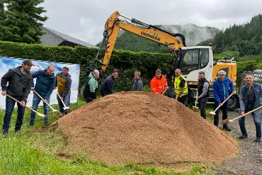 Elf Männer stehen um einen großen Sandhaufen und setzen ihre Spaten an