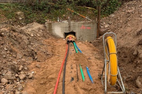 In einem Graben liegen verschiedene Rohrleitungen, die aus einer betonierten Unterführung unter einem Bahndamm entspringen