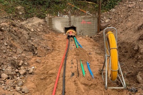 In einem Graben liegen verschiedene Rohrleitungen, die aus einer betonierten Unterführung unter Schienen entspringen