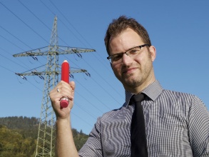 Armin Komenda mit übergroßem Rotstift, im Hintergrund eine Hochspannungsleitung