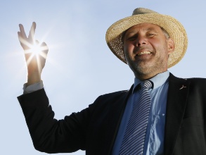 Mann mit Strohut macht eine Okay-Geste, die von Sonnenstrahlen durchleuchtet wird