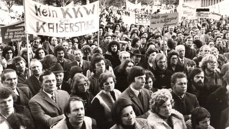 Archivaufnahme einer Demonstration gegen Atomkraftwerke in Wyhl, ein großes Transparent zeigt die Aufschrift "Kein KKW am Kaiserstuhl" 