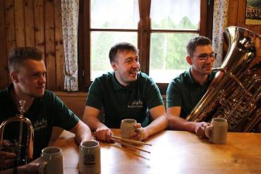 Drei Menschen mit Blasinstrumenten sitzen an einem Tisch, auf dem Bierkrüge stehen.