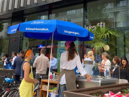 Vor dem EWS Store im Volksbankgebäude ist unter einem großen Schirm ein Eis-Verkaufsstand aufgebaut, der von hinten zu sehen ist, davor warten eine Menge Menschen an