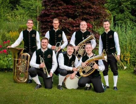 Eine Gruppe von Menschen mit Blasinstrumenten steht auf einer Wiese.