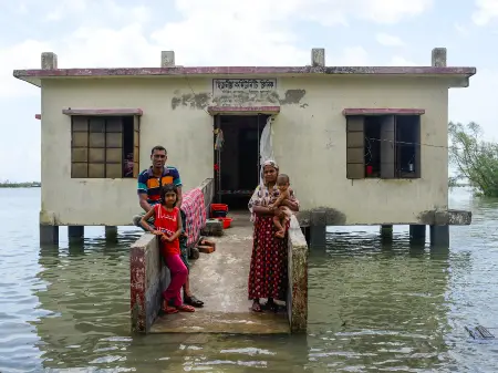 Eine pakistanische Familie steht am Eingang eines kleinen Hauses, das komplett im Wasser steht