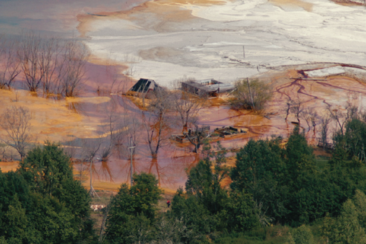 Stellenweise braun verfärbter See, aus dem einzelne Dächer herausragen
