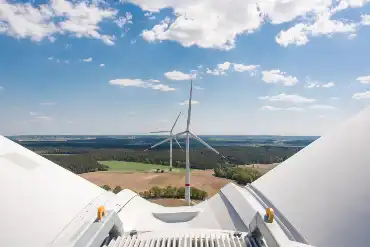 Blick von der Kuppel einer Windradkraftanlage, im Bild sind zwei Rotorenblätter, darunter erstreckt sich eine weite, flache Landschaft mit zwei weiteren Anlagen