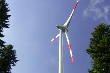 Einzelne Windkraftanlage vor blauem Himmel und einzelnen Bäumen