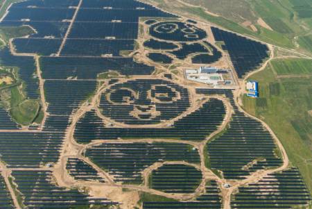 Luftbild eines riesigen Solarparks: Die hellen Wege zwischen den dunklen PV-Modulen bilden die Umrisse zweier Pandas ab..