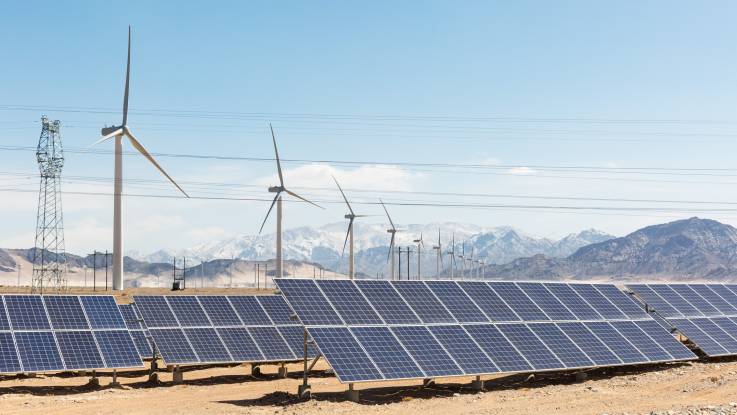 Ein Solar- und Windpark in einer Wüstengegend, durchzogen von einer Hochspannungstrasse; im Hintergrund schneebedeckte Berge
