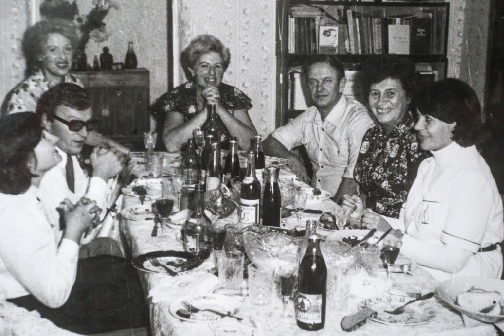 Ein zerkratztes Schwarzweißfoto zeigt eine fröhliche Geburtstagsgesellschaft am Tisch