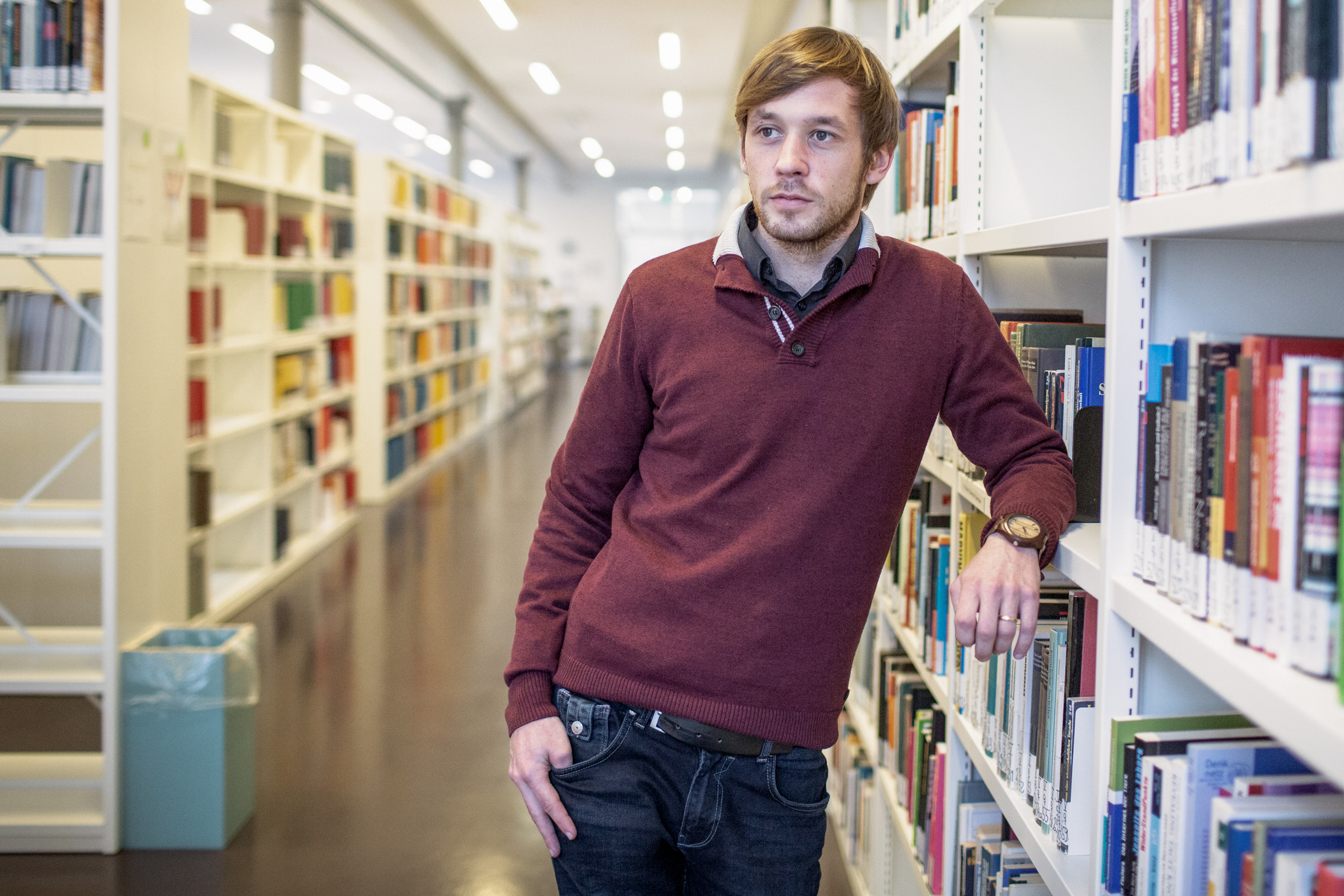 Junger Mann lehnt am Bücherregal und schuat nach links