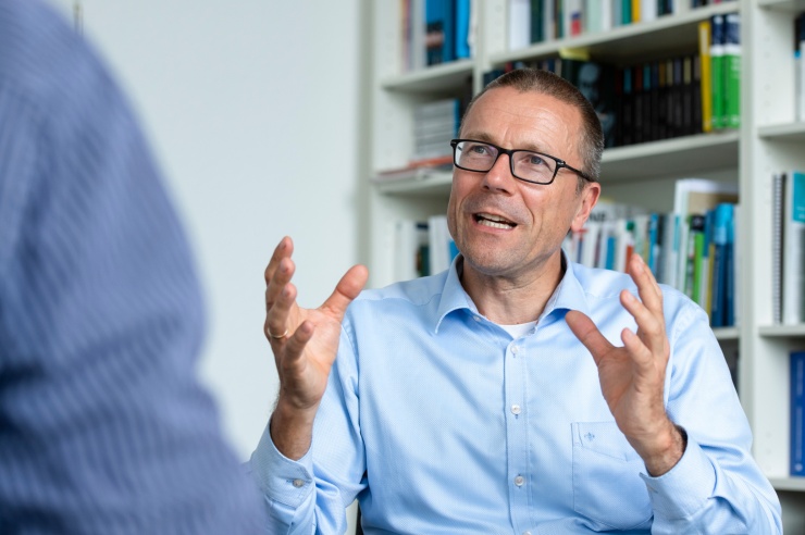 Mann mittleren Alters vor einer Bücherwand im Gespräch