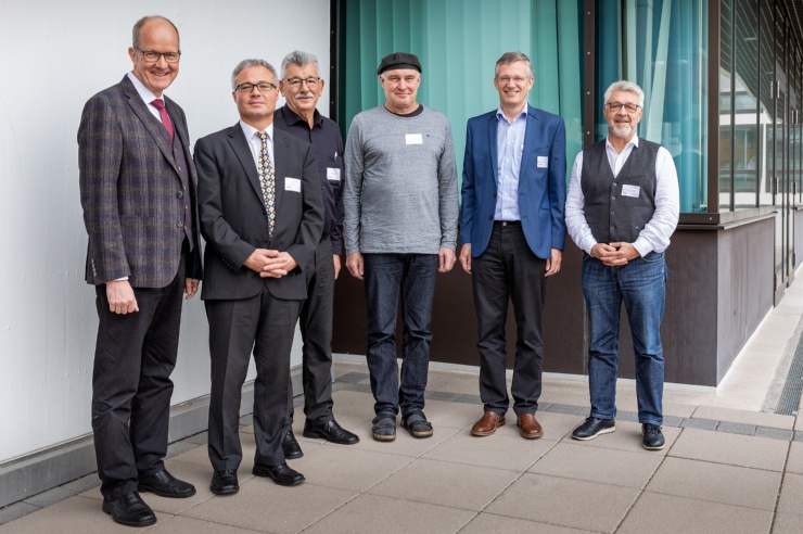 Eine Gruppe von sechs Männern stehen aufgereiht  draußen, in einer Hausecke fotografiert.