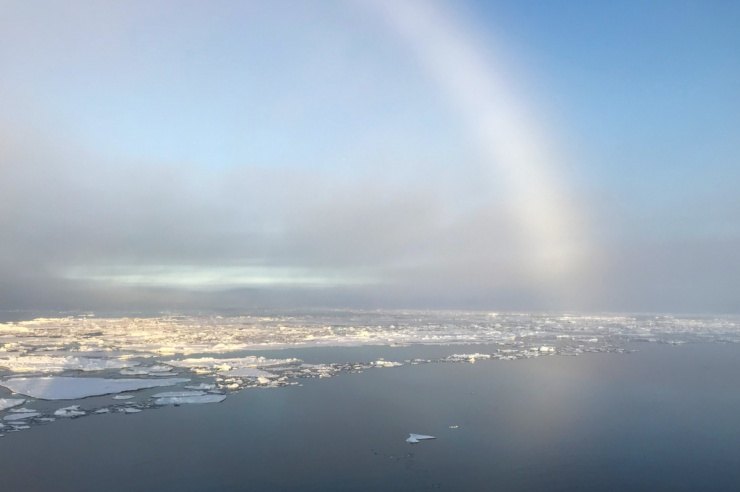 Blick aufs Meer, im Hintergrund ein Regenbogen. Auf dem Meer viele kleine Eisschollen.