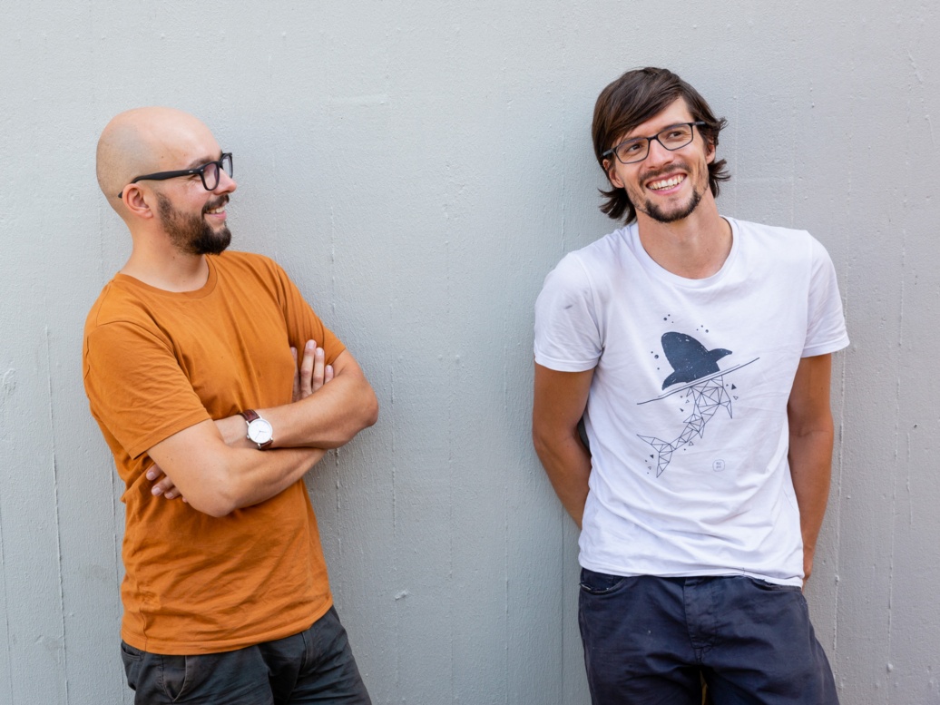 Zwei junge Männer im Sommer, lachend vor einer Wand