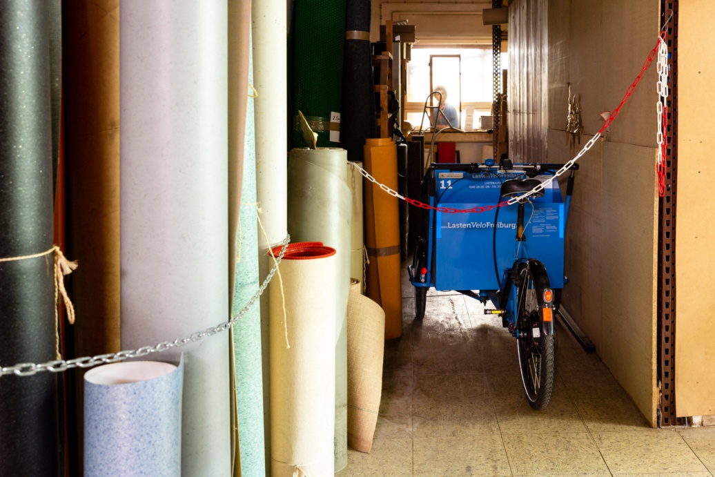 Ein Lastenrad steht geparkt neben Teppichrollen.