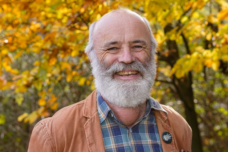 In einem herbstlichen Wald steht ein freundlicher Mann schaut lachend in die Kamera.