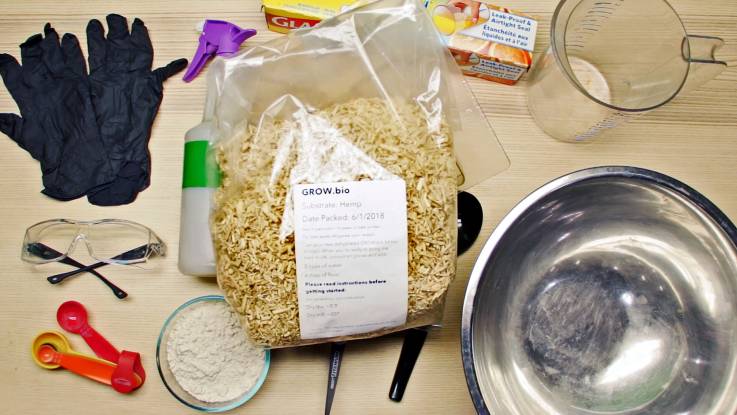 Auf einem Tisch sind Handschuhe, eine Schutzbrille, Messlöffel, eine Schale mit weißlichem Pulver, eine Sprühflasche, ein Beutel faseriges Material, eine Tube Abdichtpaste sowie ein Messbecher und eine kleine Edelstahlschüssel ausgebreitet.