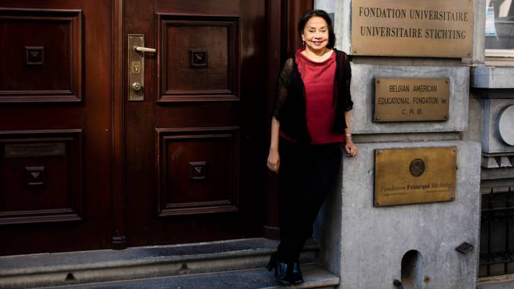 Frau Guha-Sapir steht draußen auf den Stufen vor einer herrschaftlichen Eingangstür.
