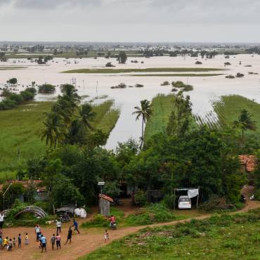Eine Fläche mit Feldern und Häusern ist weitläufig überschwemmt. Einige höher gelegene Häuser stehen im Trockenen.