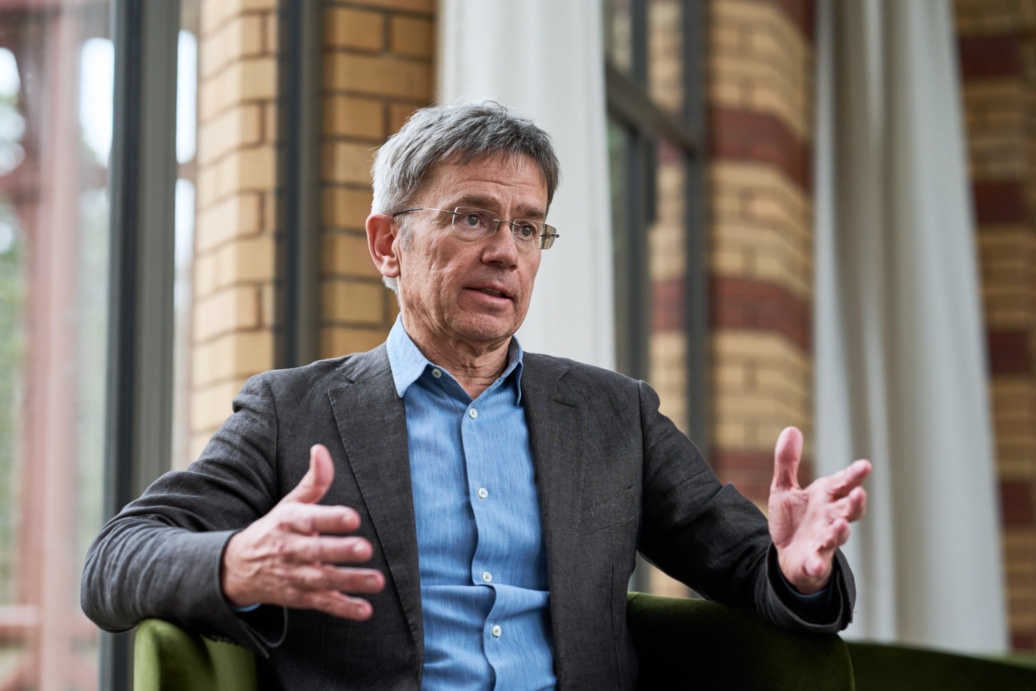Ein Mann mittleren Alters, im Anzug, sitzt im Gespräch vor einer Fensterfront.