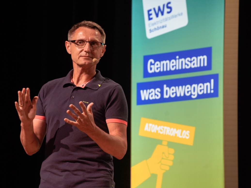 Vor einer grün-gelben Stele mit dem Slogan 