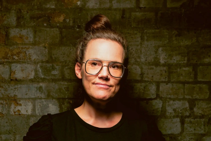 Porträtaufnahme: Katja Diehl lächelt, trägt ein rotes T-Shirt und hat ihre Haare zum Dutt hochgebunden. 