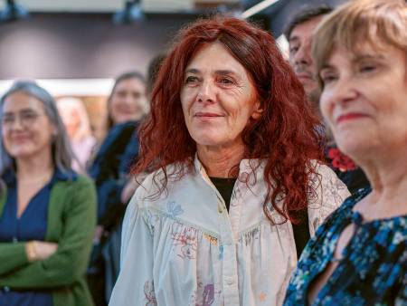 Die Frau mit den roten Haaren steht mit anderen Personen in einer Galerie und hat ein sanftes Lächeln im Gesicht.