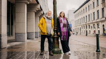 A man with gray hair and a younger woman with light brown hair lean against a green lantern.