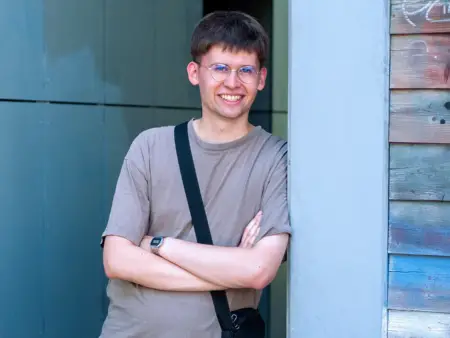Ein junger Mann im T-Shirt steht mit verschränkten Armen angelehnt an eine Wand, die mit Graffiti besprüht.