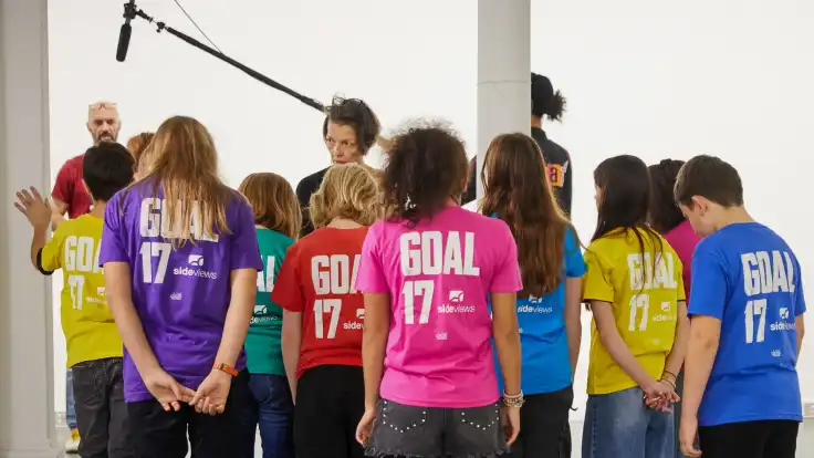 Die Gruppe ist nun von hinten zu sehen: auf der Rückseite ihrer T-Shirts steht in Versalien „Goal 17“ geschrieben.